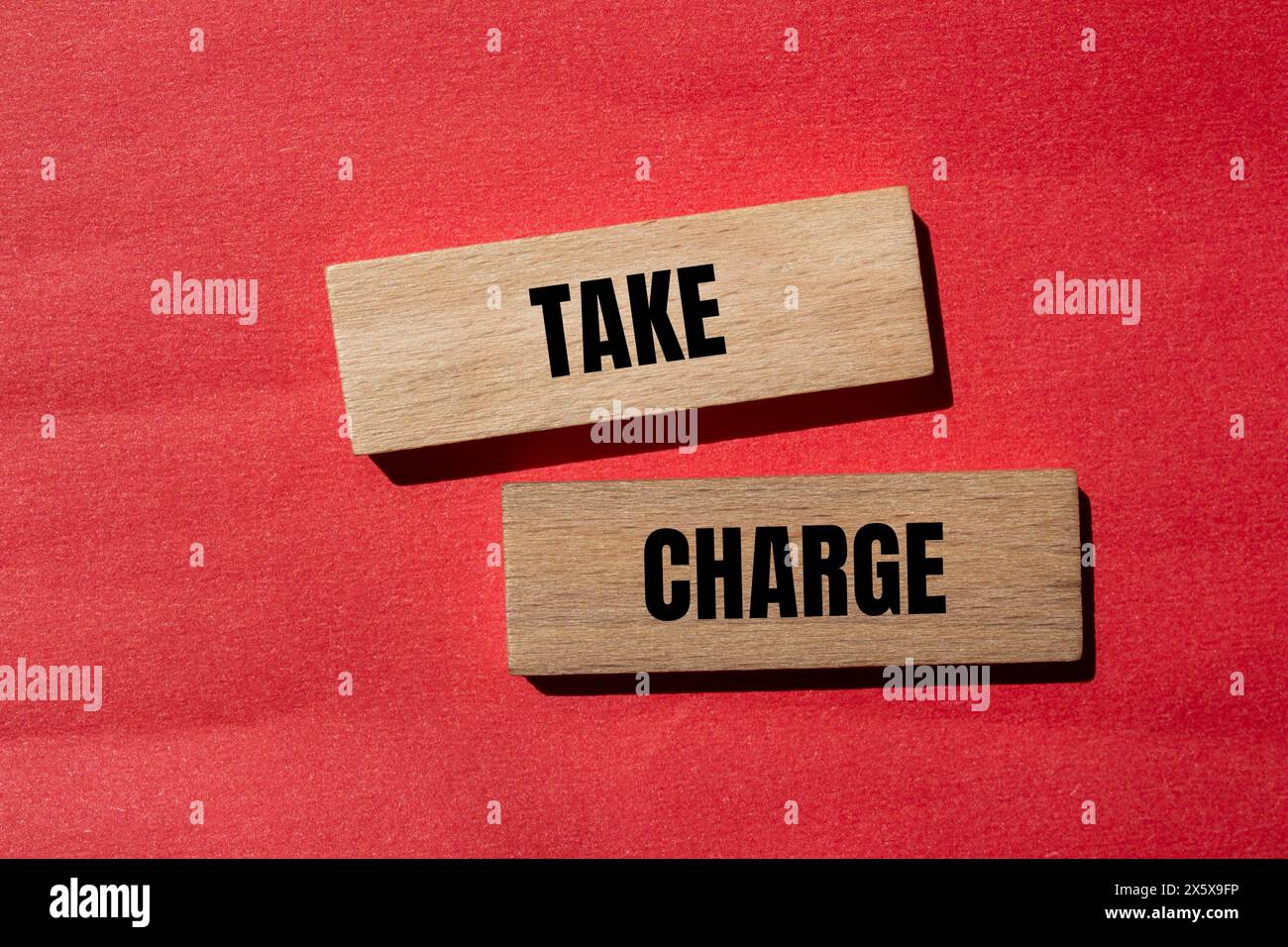 Take charge words written on wooden blocks with red background. Conceptual take charge symbol. Copy space. Stock Photo