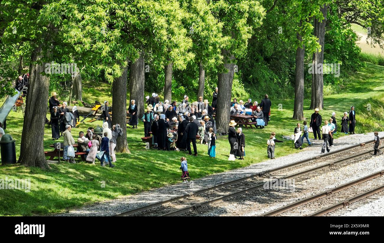 An Amish Community Gathering in a Shaded Park by Railroad Tracks Stock Photo