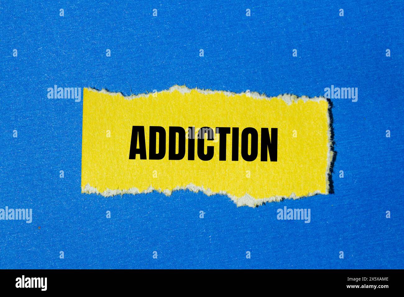 Addiction word written on ripped yellow paper with blue background. Conceptual addiction symbol. Copy space. Stock Photo