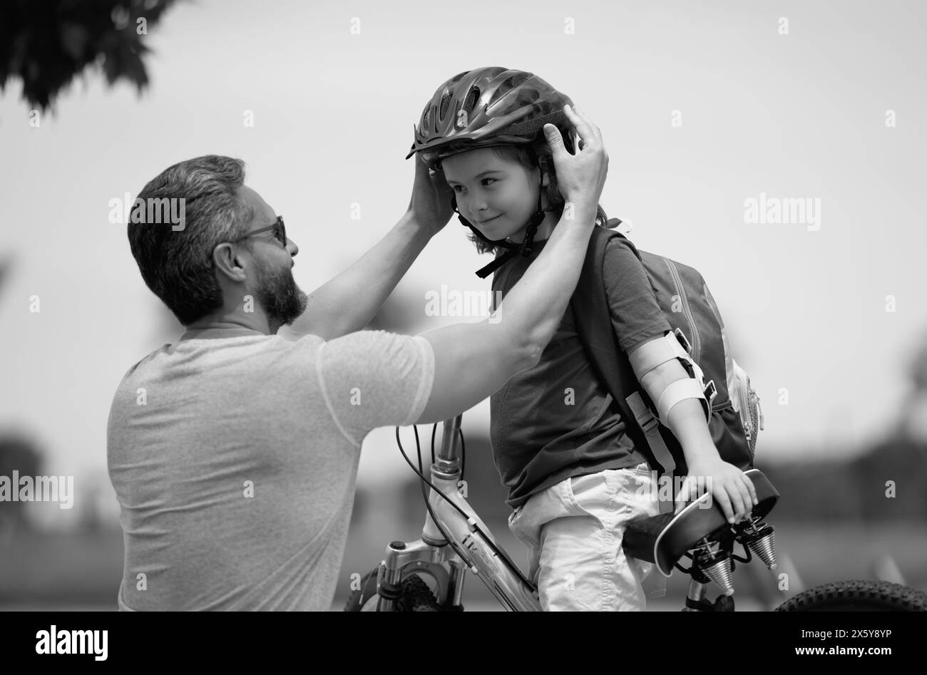 Little kid learning to ride bicycle with father in park. Father teaching son cycling. Father and son learning to ride a bicycle at Fathers day. Father Stock Photo