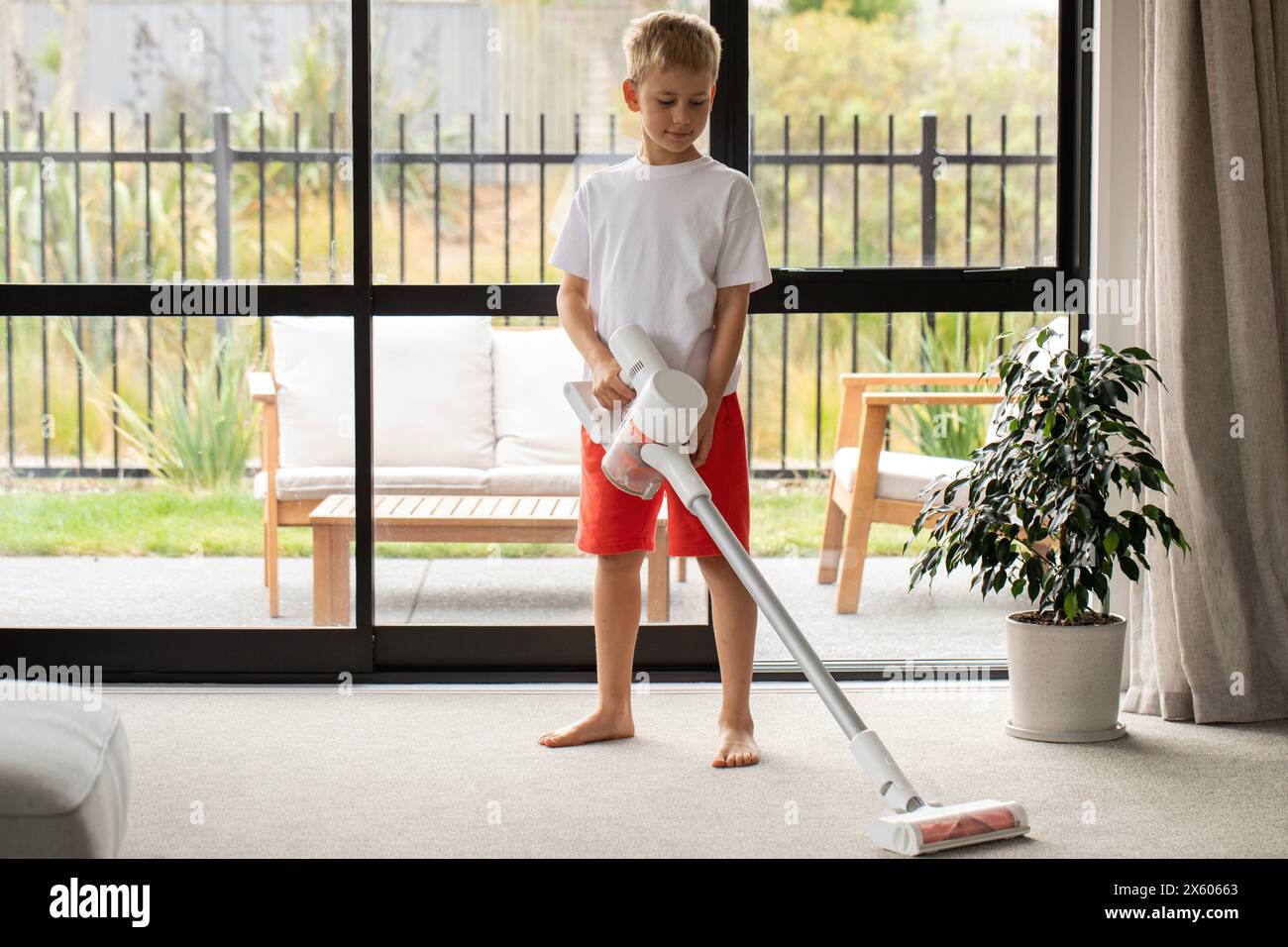 A boy vacuums the living room with a modern wireless vacuum cleaner ...