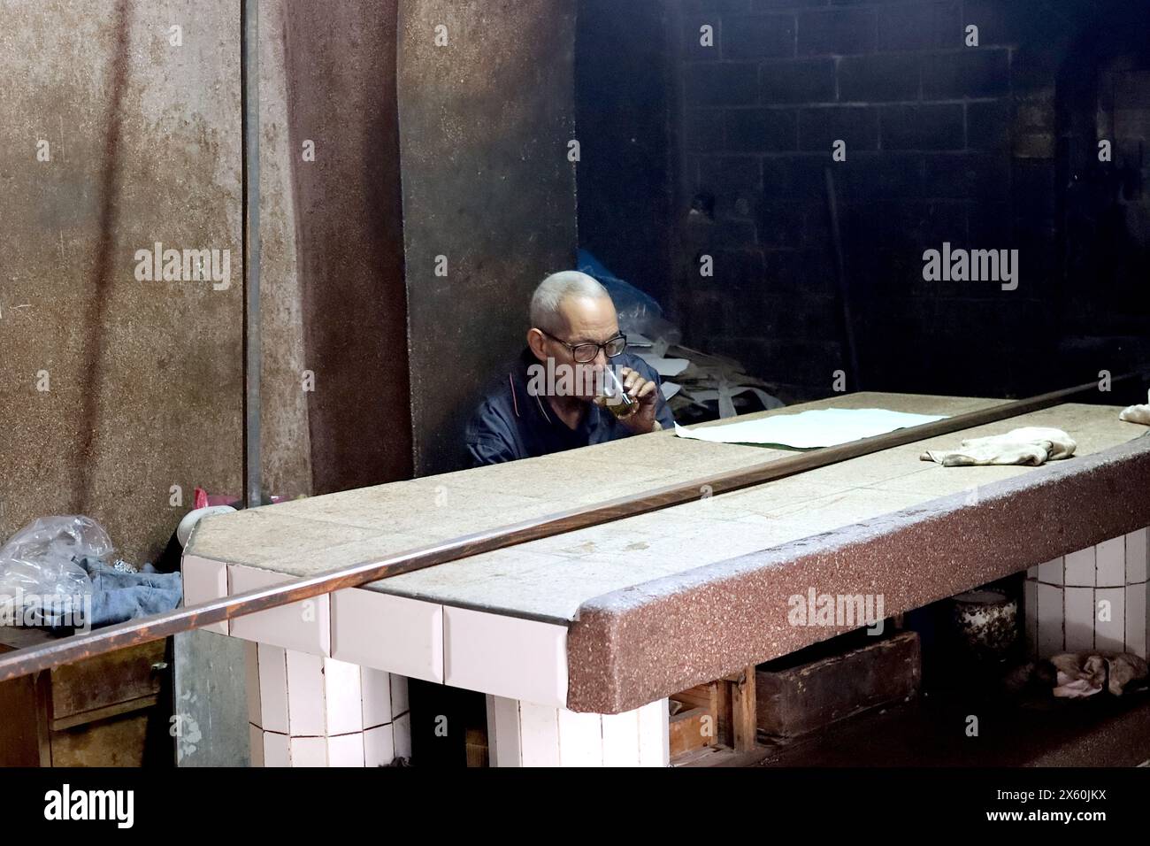 In almost total darkness, a Moroccan baker takes a break, waiting for the next customer at communal ovens in Casablanca, April 2024. Stock Photo