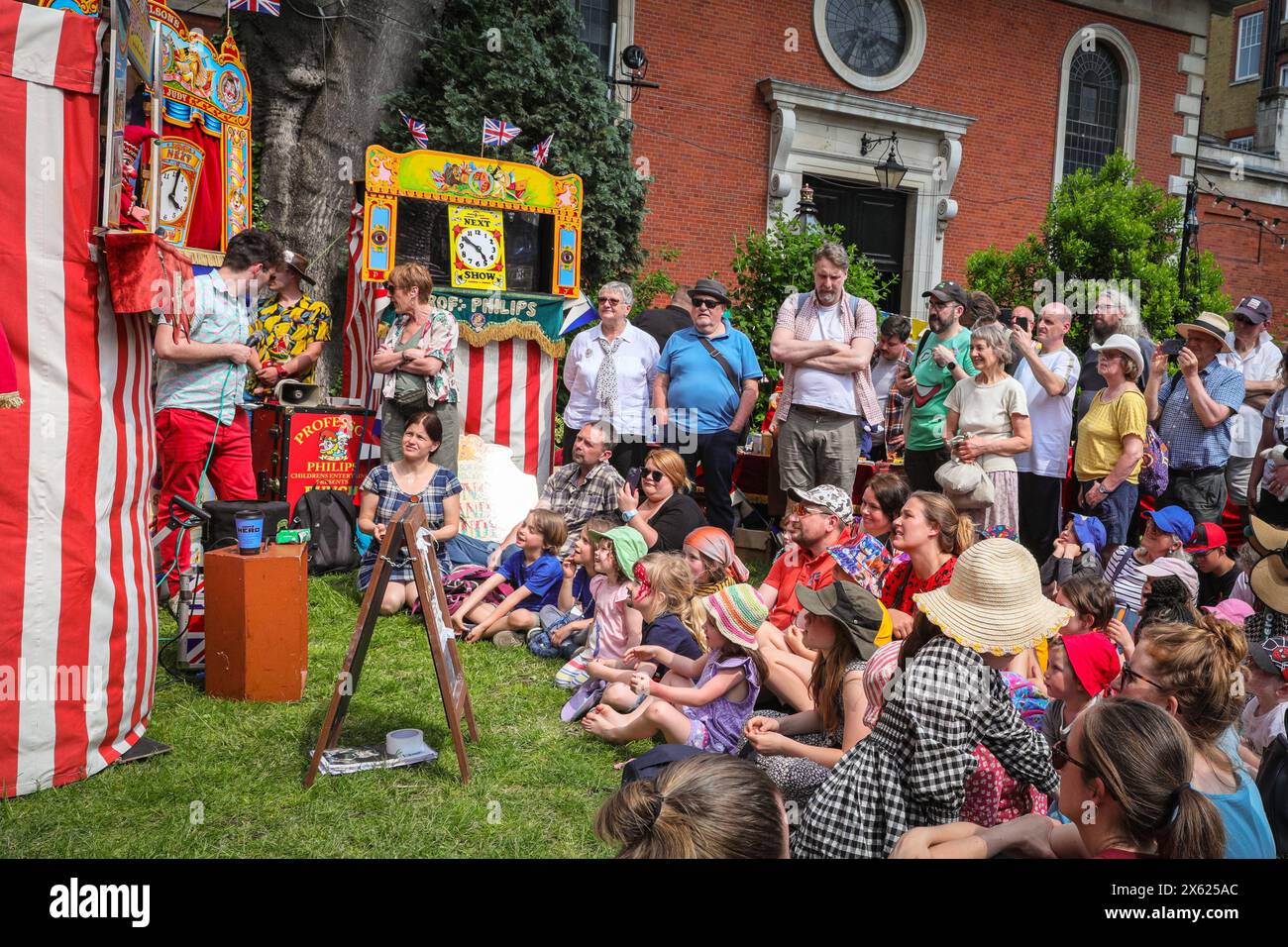 London, UK. 12th May, 2024. Kids and adults watch a show by one of the members of the Punch & Judy Fellowship. The afternoon seen a number of traditional and modern Punch and Judy shows entertain the crowds. Puppeteers from across the country gather for the annual May Fayre and Puppet Festival. It takes place in the grounds of St Paul's Church (also called The Actor's Church), Covent Garden and includes a church service, procession, Punch and Judy shows, workshops, stalls and family fun. Credit: Imageplotter/Alamy Live News Stock Photo