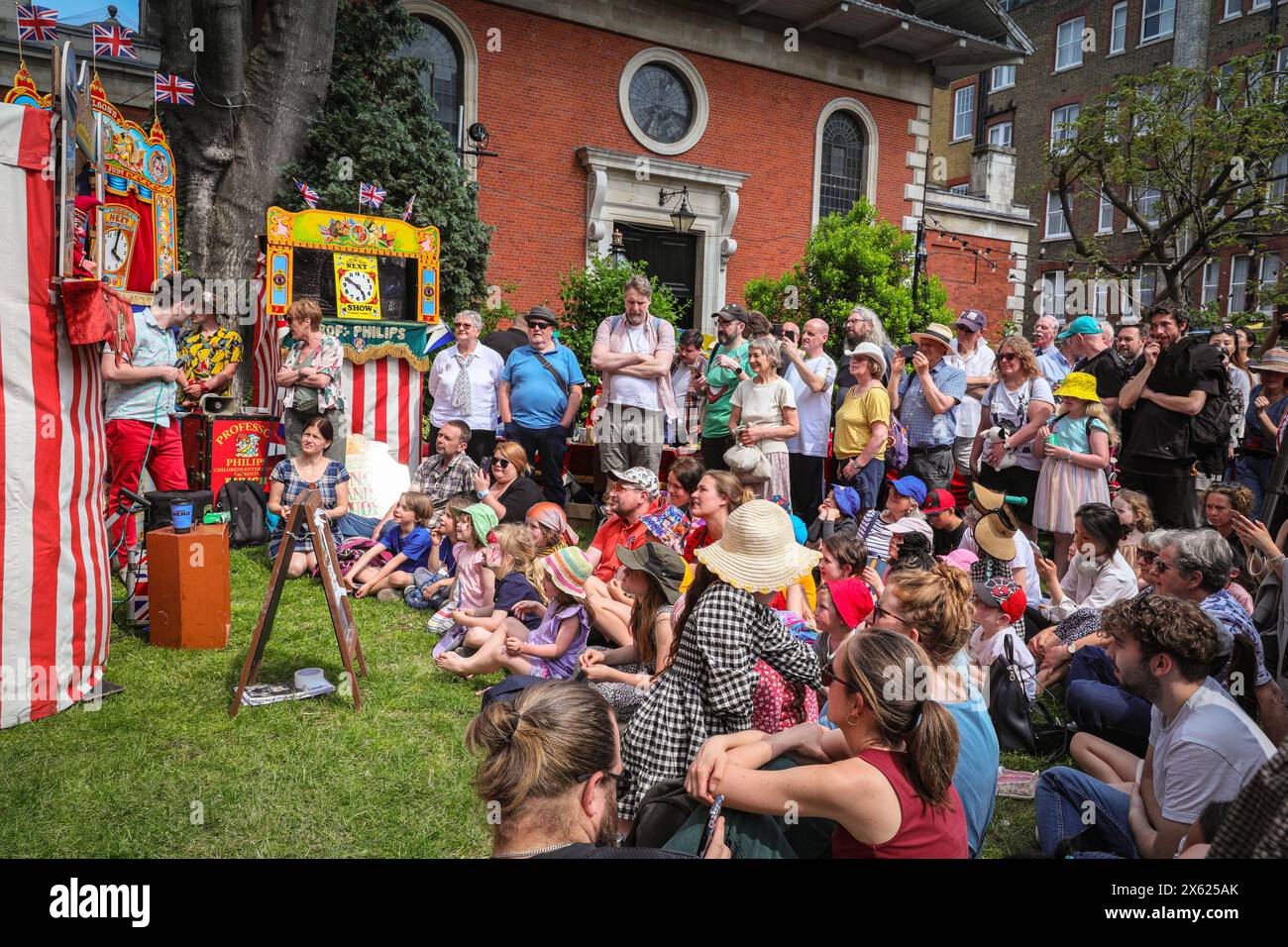 London, UK. 12th May, 2024. Kids and adults watch a show by one of the members of the Punch & Judy Fellowship. The afternoon seen a number of traditional and modern Punch and Judy shows entertain the crowds. Puppeteers from across the country gather for the annual May Fayre and Puppet Festival. It takes place in the grounds of St Paul's Church (also called The Actor's Church), Covent Garden and includes a church service, procession, Punch and Judy shows, workshops, stalls and family fun. Credit: Imageplotter/Alamy Live News Stock Photo
