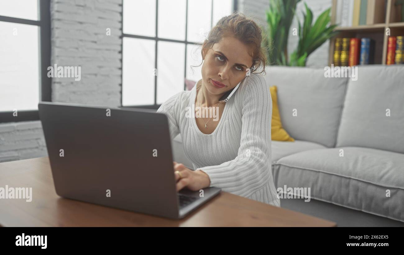 A thoughtful young woman multitasks with a phone call and laptop in a ...