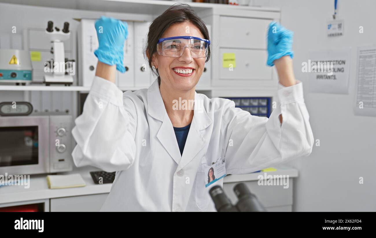 A smiling hispanic woman donning lab coat and safety goggles poses