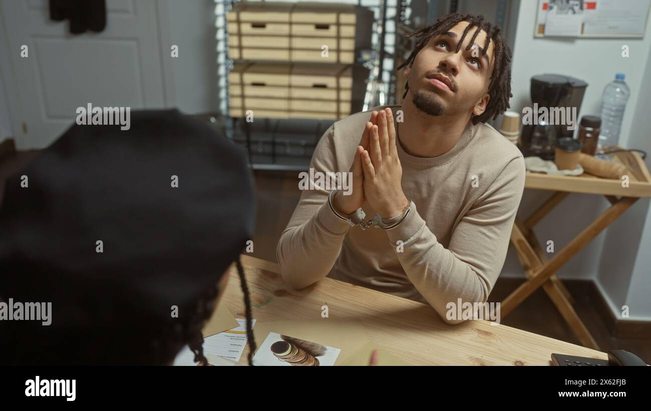 Interrogation scene with handcuffed man looking up at a detective in a police room with evidence on the table. Stock Photo