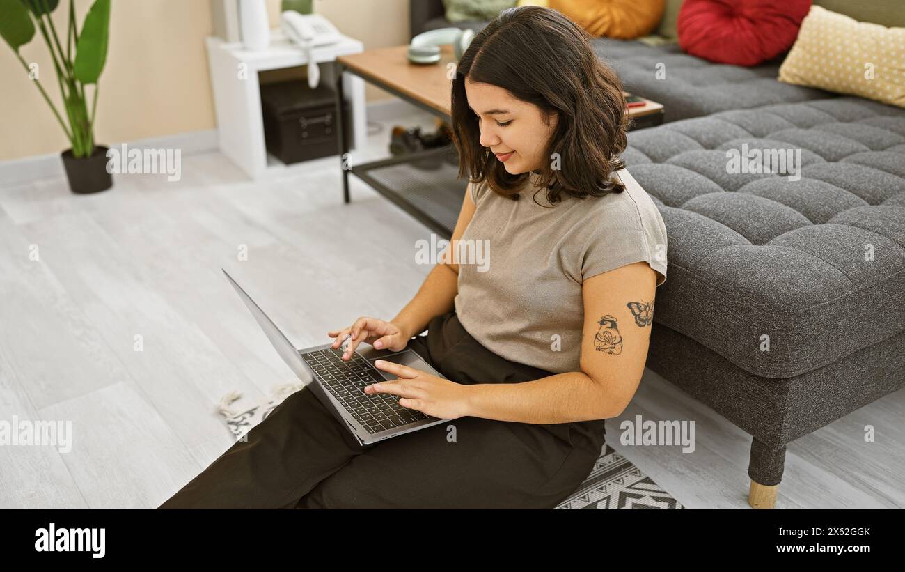 Hispanic woman working on laptop in modern apartment living room. Stock Photo