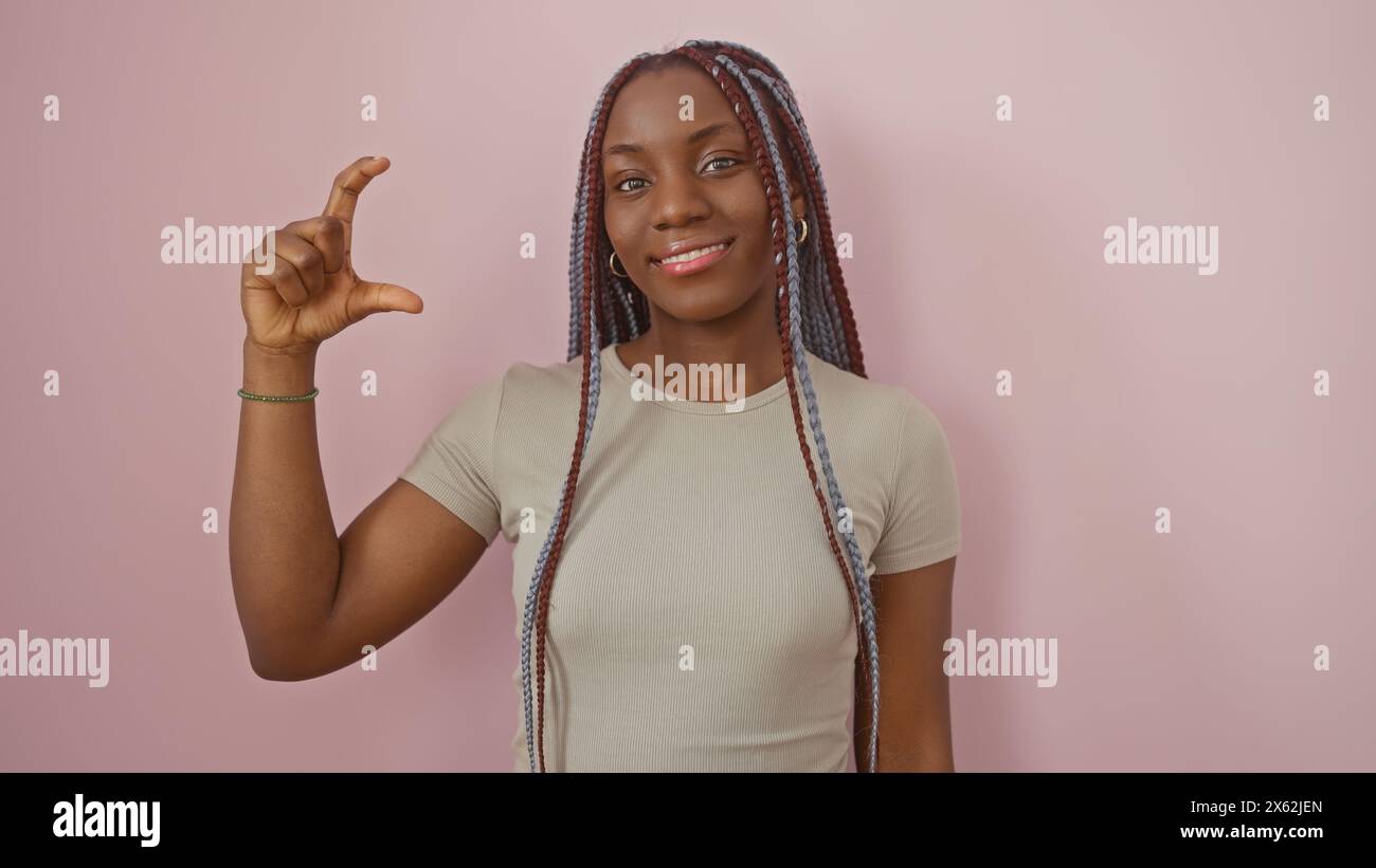 A confident african american woman with braids poses against a pink ...
