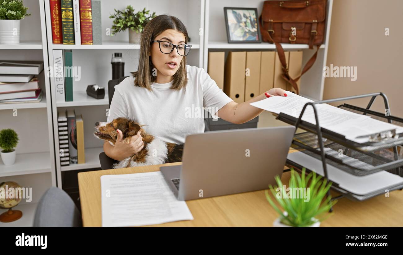 A professional hispanic woman multitasks in an office, holding a dog ...