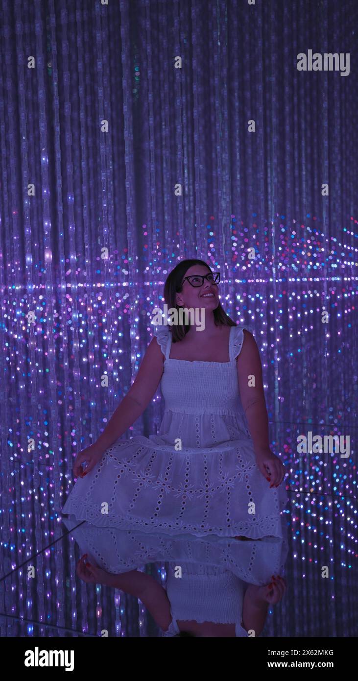 Smiling beautiful hispanic woman experiencing immersive futuristic exhibit at modern museum - lasers, lights, innovation at their best! Stock Photo