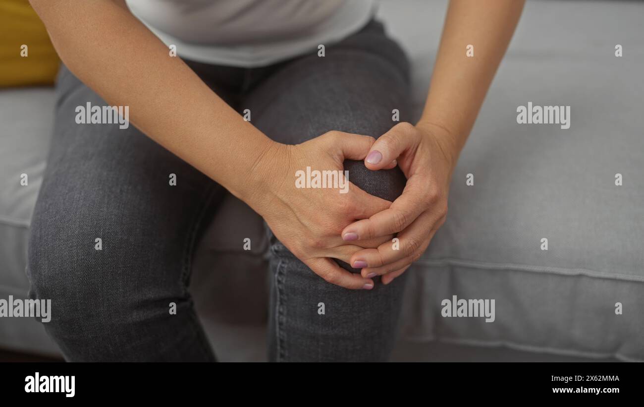 Close-up of a young woman's hands clasping her knee indoors, portraying comfort and casual style. Stock Photo