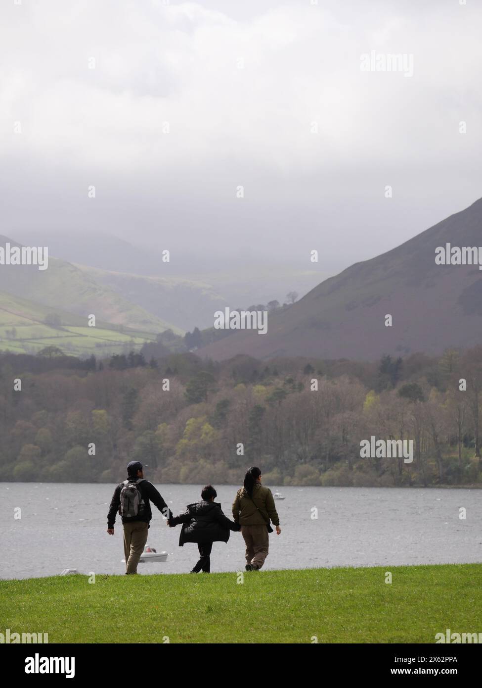 Young family holding hands and walking alongside Lake. Derwentwater, Lake District, Cumbria, UK Stock Photo
