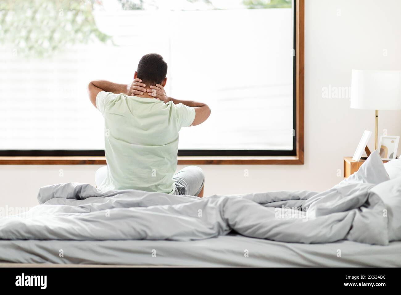 Man Enjoying Relaxing Morning Stretch in a Bright, Sunlit Bedroom Stock Photo