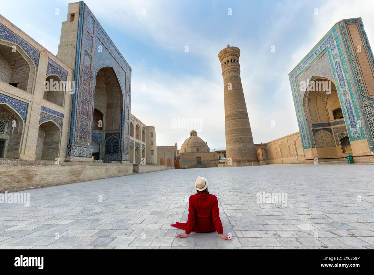 Tourist woman with hat and red dress sitting on Poi Kalyon square an ancient public square in the heart of the ancient city of Bukhara, Uzbekistan. Stock Photo