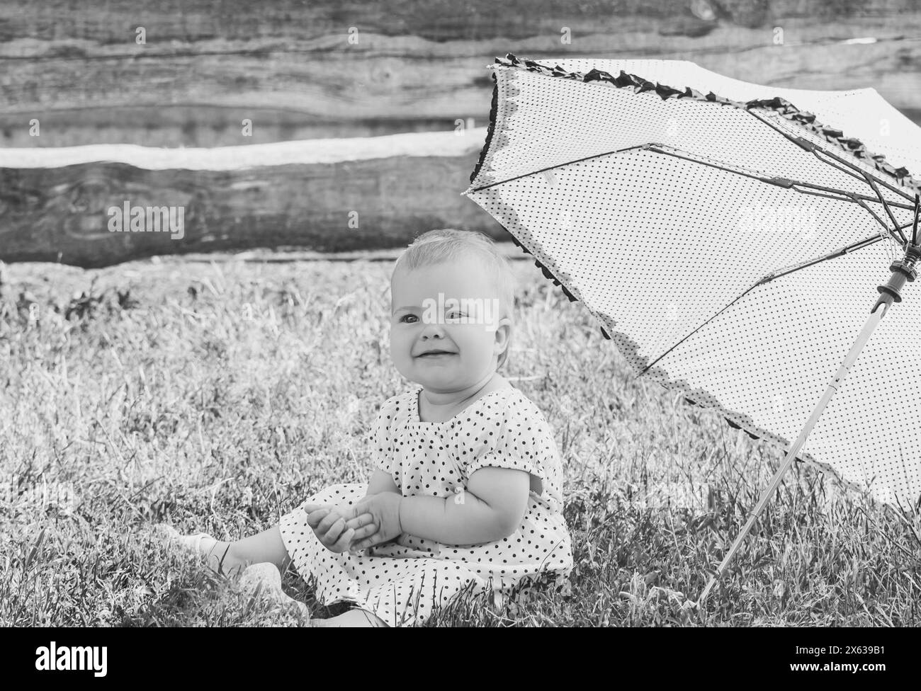 beautiful baby in a polka-dot dress is sitting nea umbrella umbrella Stock Photo
