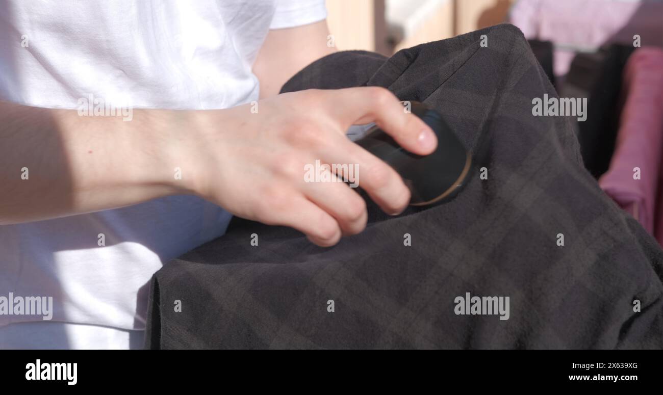 Experience ultimate in garment care as stylish man meticulously removes lint from his shirt using specialized handheld device Perfect showcasing Stock Photo