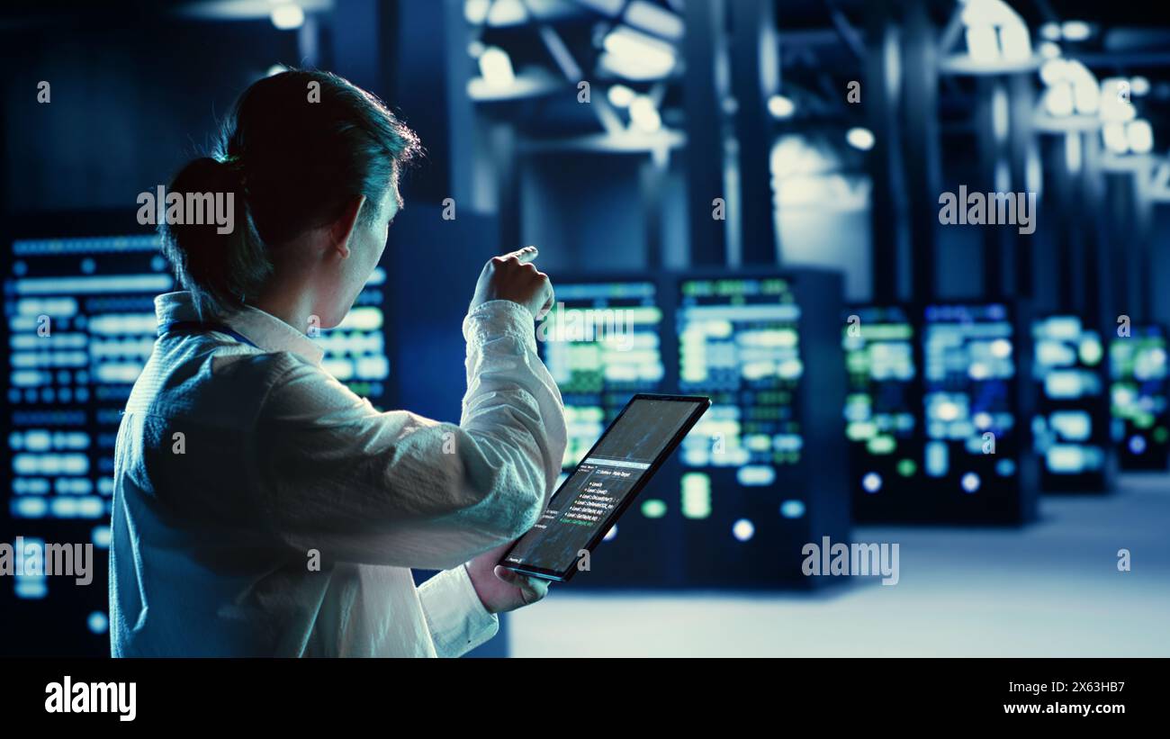 Trained asian admin running code and programming on tablet, troubleshooting and upgrading high tech facility equipment designed to accommodate servers, networking systems and storage arrays Stock Photo