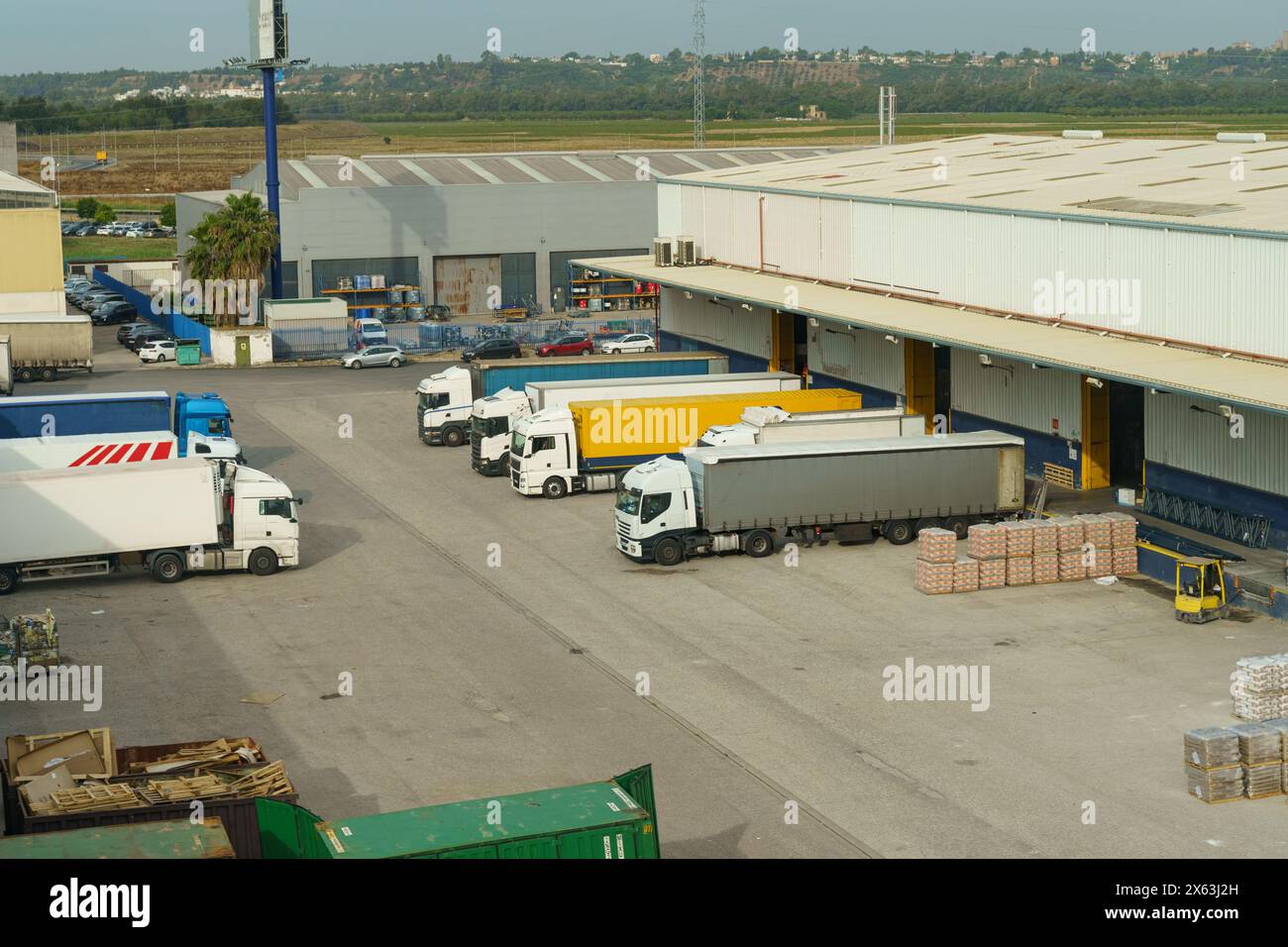Multiple trucks of varying sizes and colors are parked neatly in rows in a large parking lot dedicated to transport and logistics operations. Stock Photo