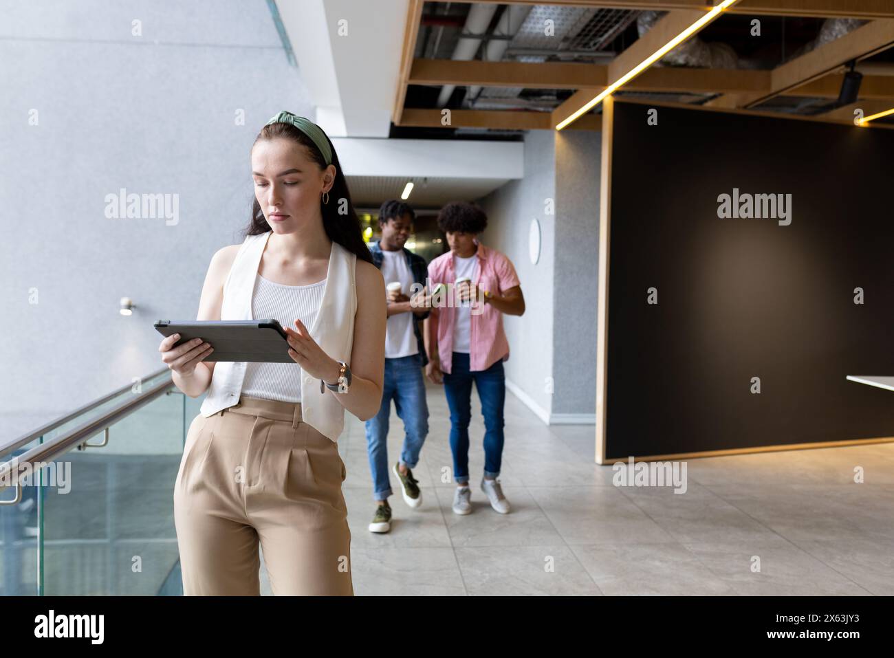 Diverse young team, Caucasian woman with tablet, walks in modern office, copy space Stock Photo