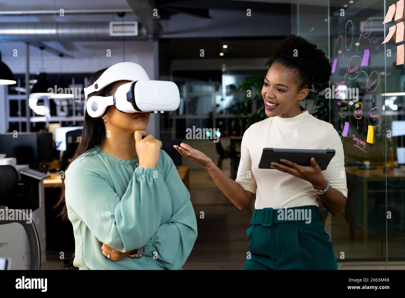 Diverse female colleagues work late using VR and tablets, with black background Stock Photo