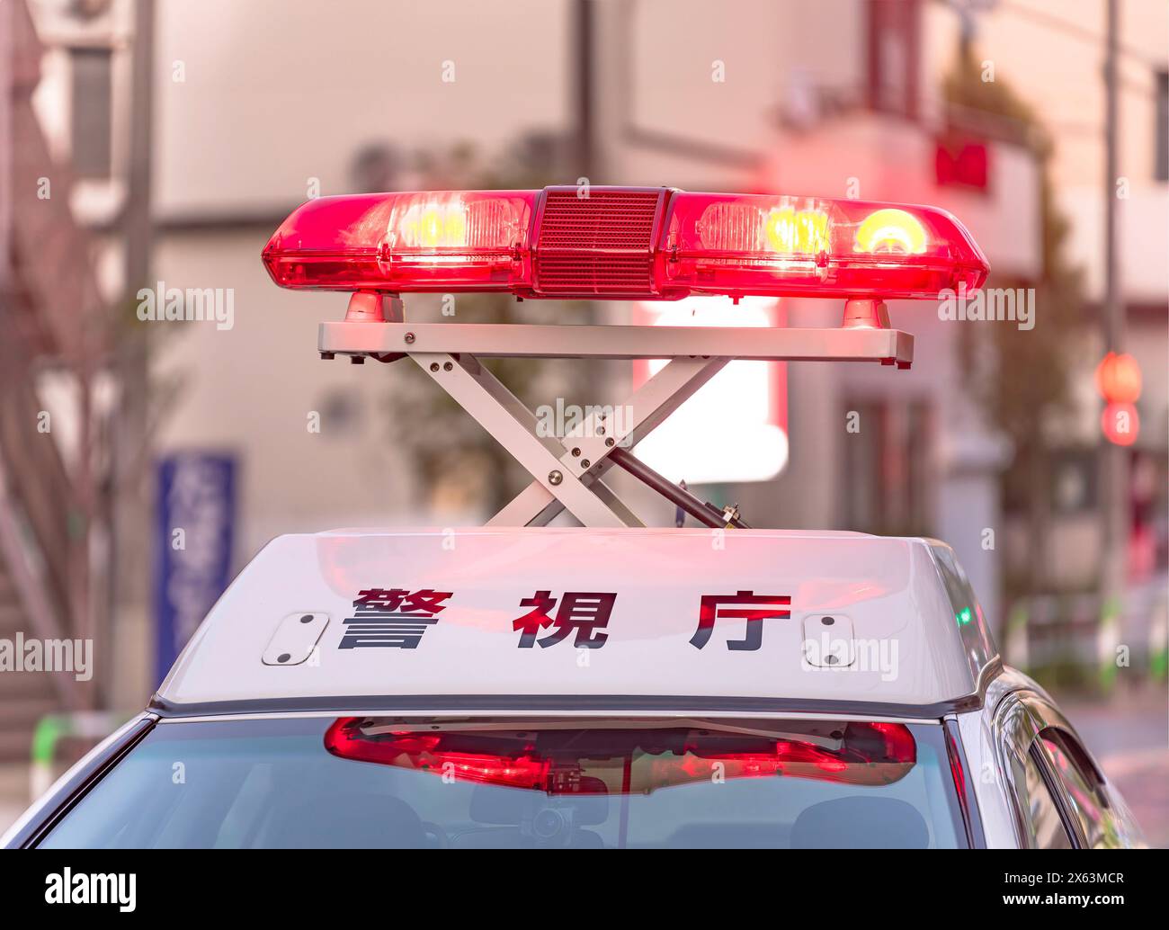 Close-up on bright red emergency beacons casting an intense glow as they swirl unfolded above the white roof of a Japanese police vehicle showing the Stock Photo