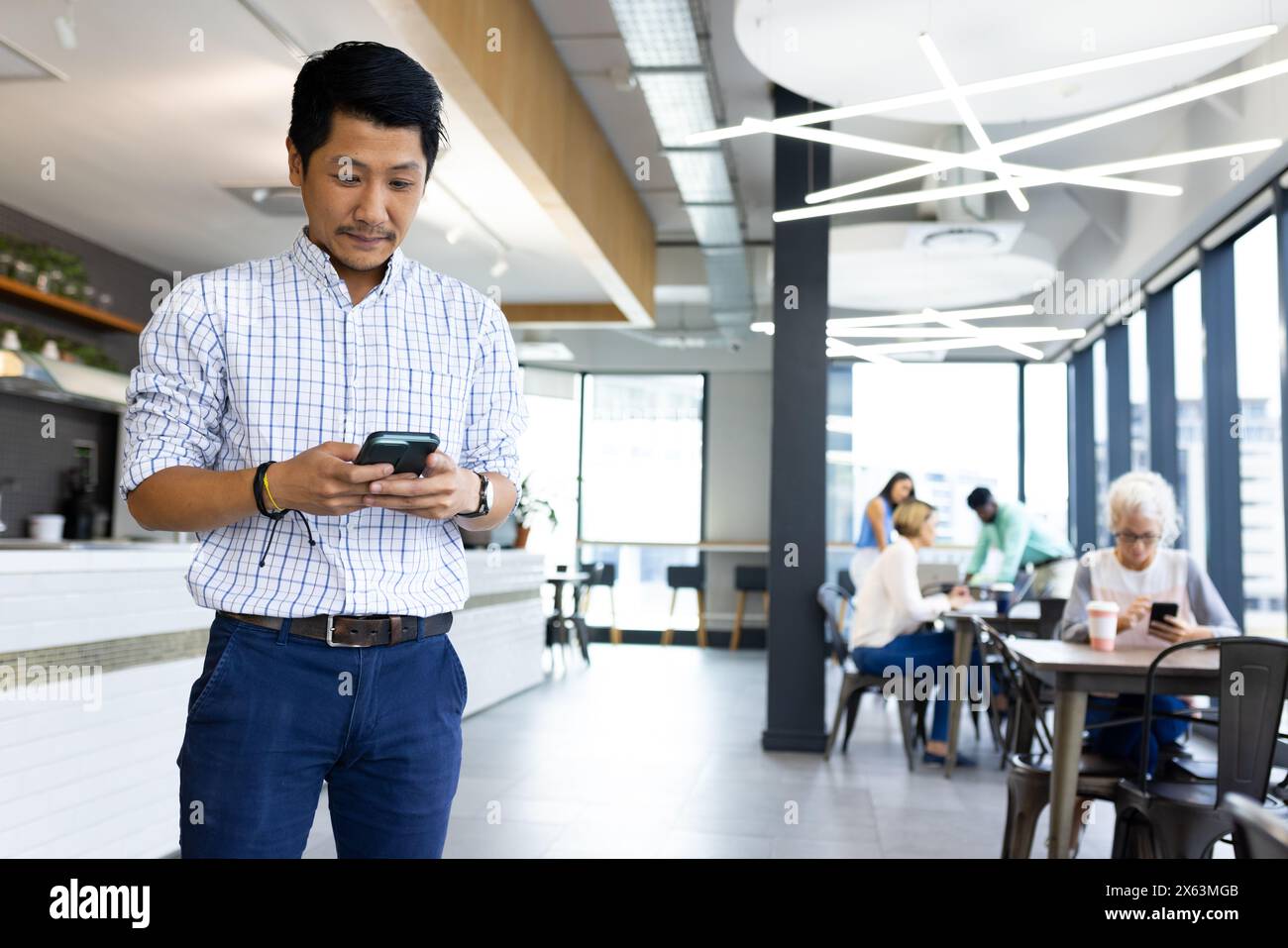 Diverse team working at office while Asian male checking smartphone in cafe Stock Photo
