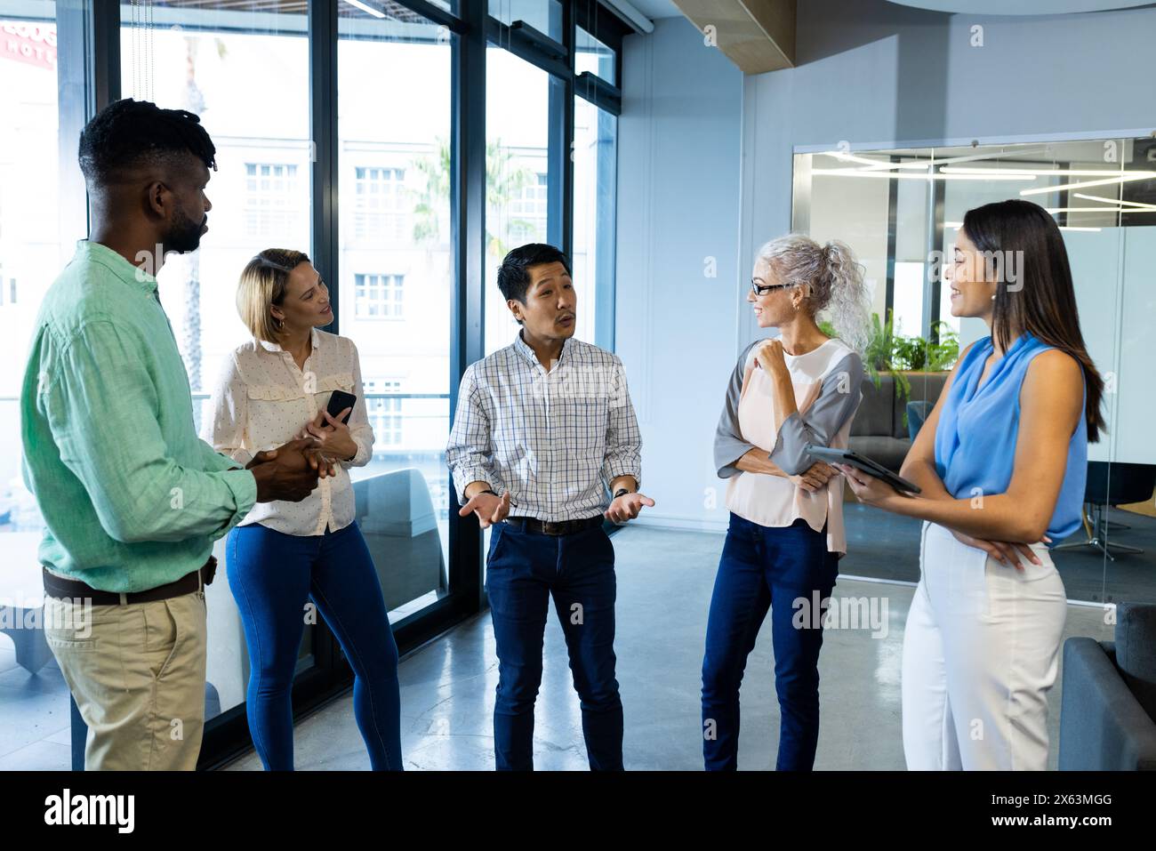 Diverse team discussing work in office, holding tablet and documents Stock Photo