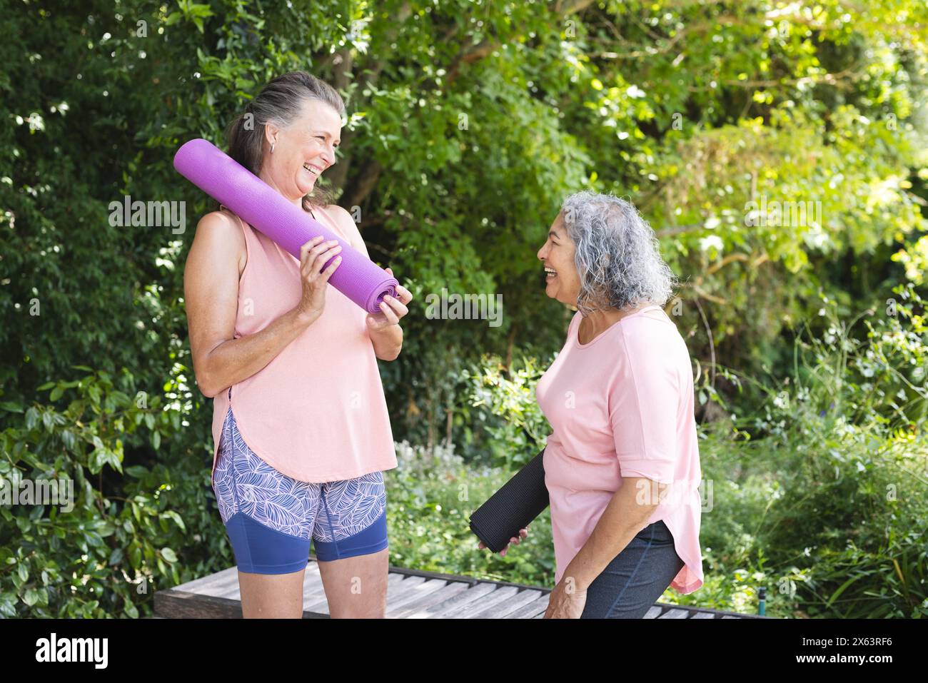 Outdoors, diverse senior female friends holding yoga mats, chatting happily Stock Photo