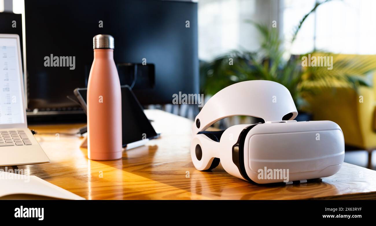 At office, VR headset resting on a wooden desk next to a laptop Stock Photo