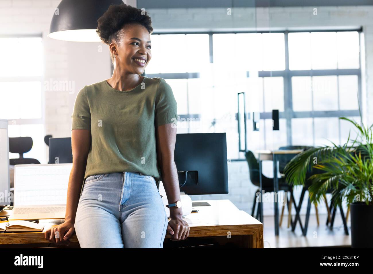At office, African American businesswoman leaning on desk, looking away Stock Photo