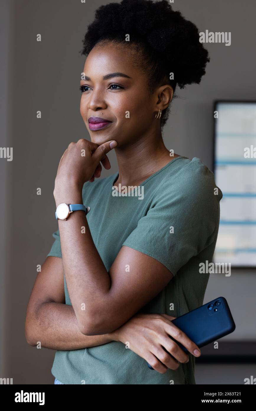At office, African American businesswoman holding smartphone, looking thoughtful Stock Photo