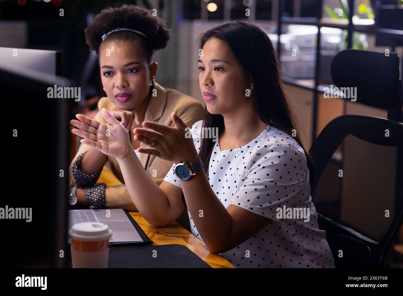 Diverse female colleagues discussing at computer, working late. African ...
