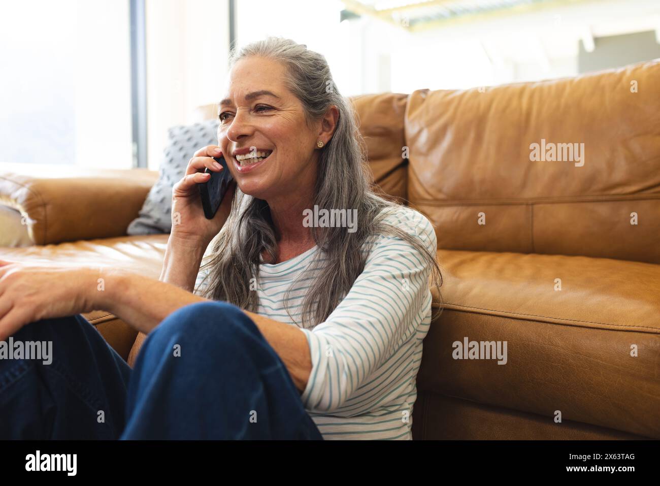 At home, mature Caucasian woman talking on a smartphone, sitting on a couch Stock Photo