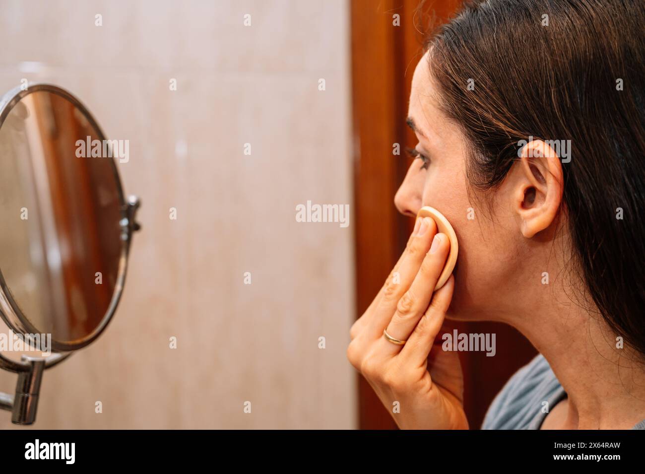 A woman is applying makeup in front of a mirror. She is using a makeup sponge to apply foundation to her face Stock Photo