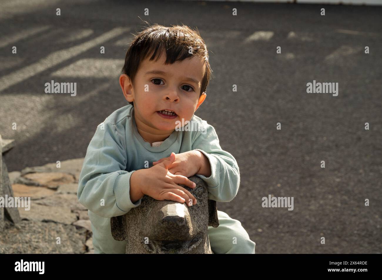 A young boy is sitting on a dog statue. He is smiling and has his hand on the statue Stock Photo