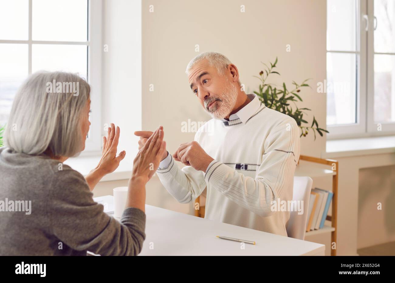 Senior couple arguing in the living room sitting at the desk at home. Stock Photo