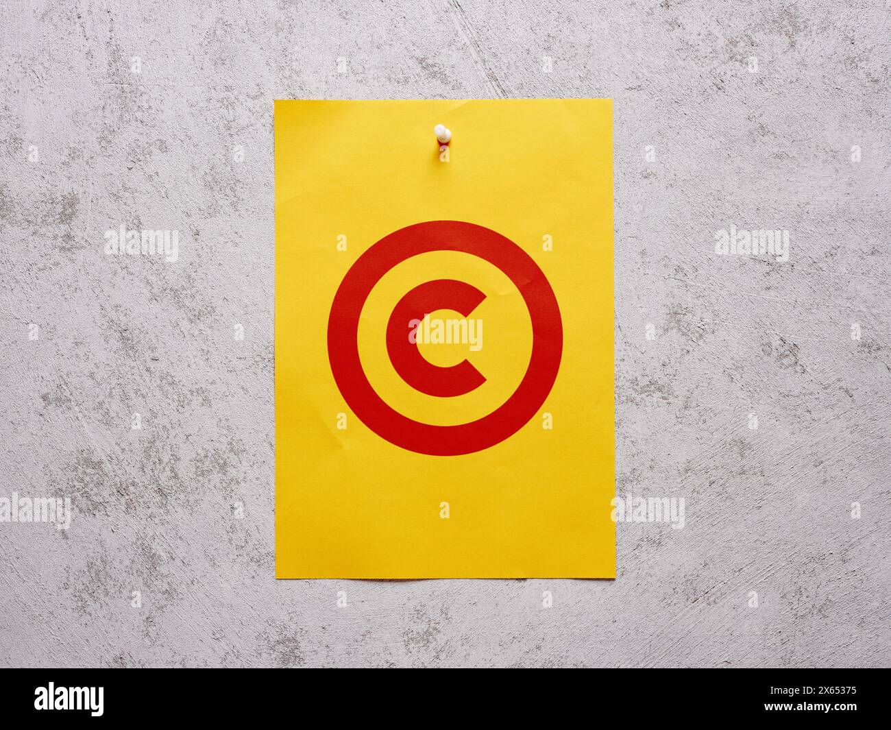 Patenting and copyright protection. Copyright symbol on a yellow sheet of paper pinned to a white concrete wall. Stock Photo