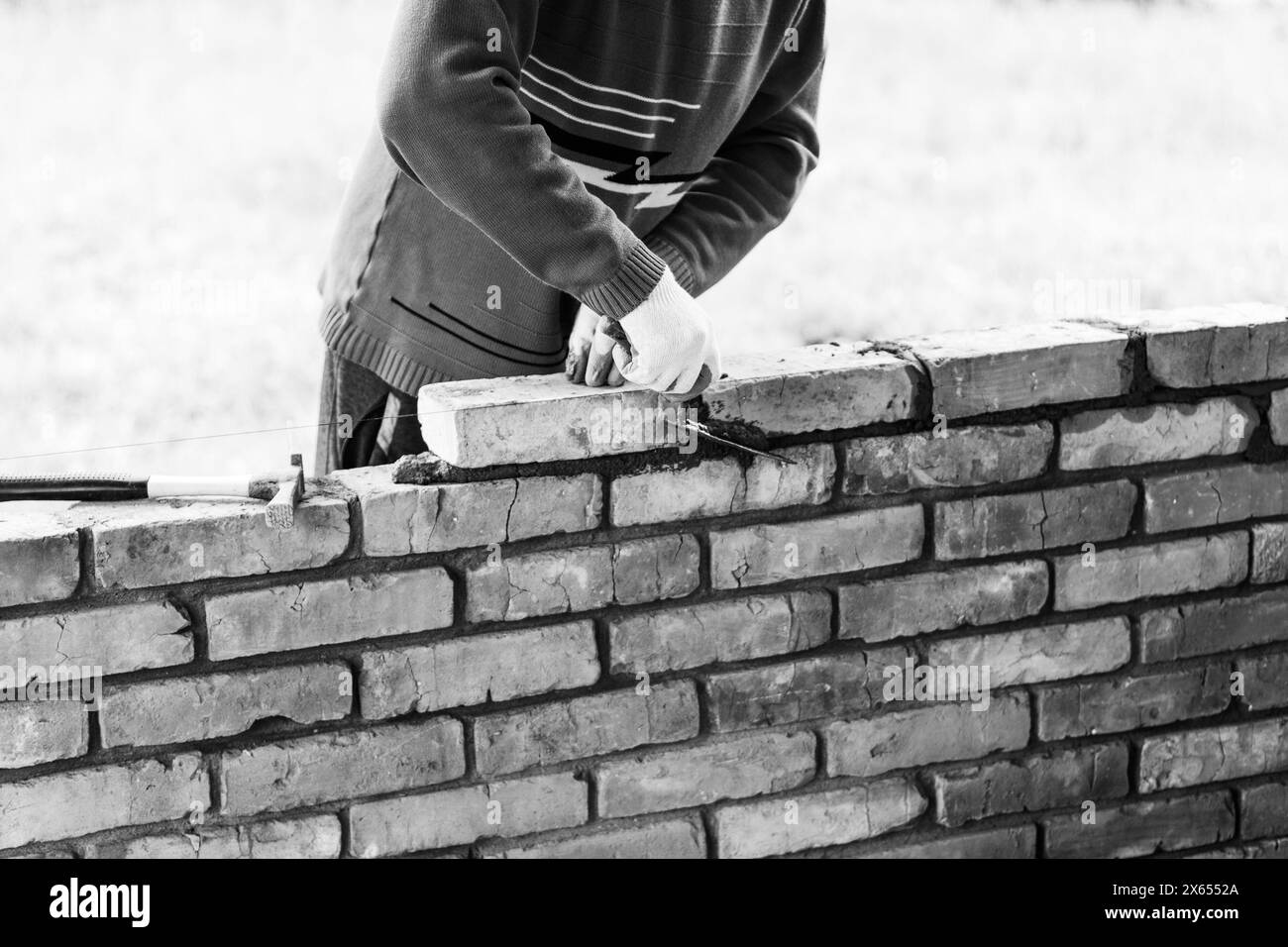 a man builds a brick wall, puts a brick on a cementsand mortar, removing excess mortar with a