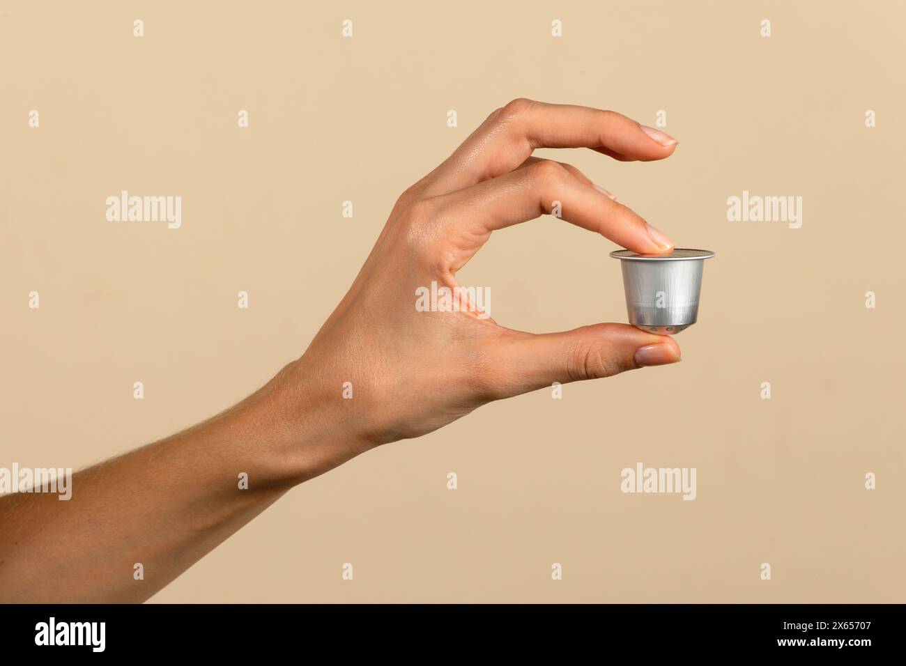 Close-up of a human hand elegantly presenting a coffee capsule, isolated on a beige backdrop Stock Photo