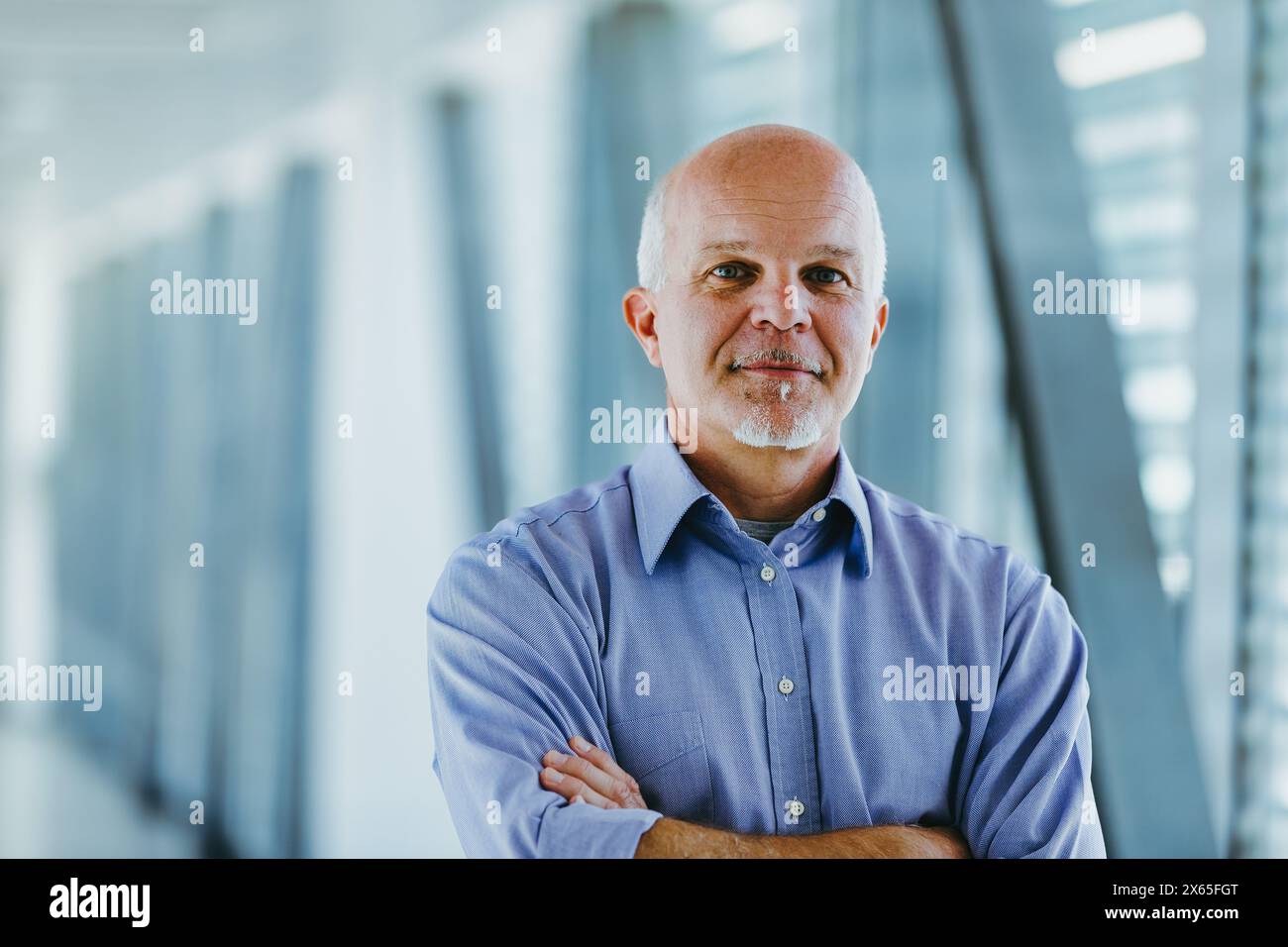 Mature man with arms crossed stands confidently in a modern office ...