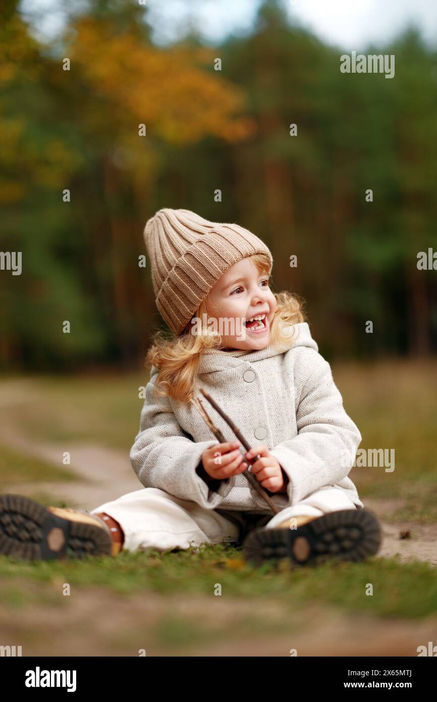 happy little girl sitting on the grass in the autumn forest at sunset Stock Photo