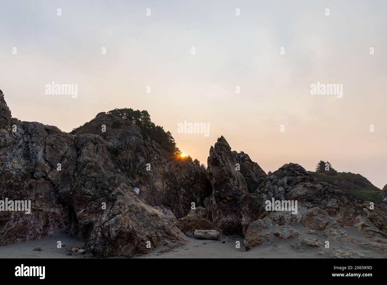 Sun peering over rocks at beach sunrise Stock Photo