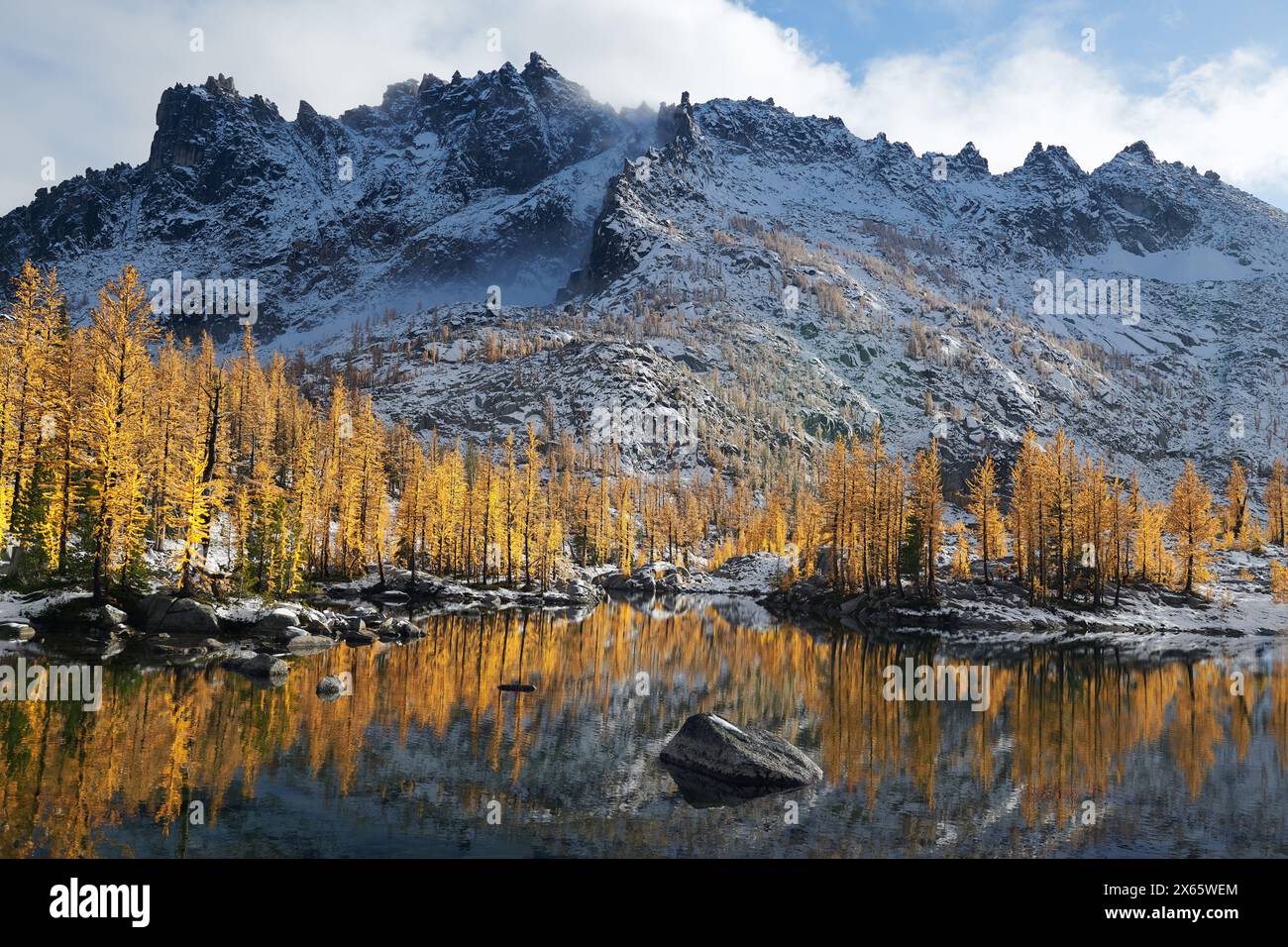 Massive mountains and yellow larches reflected in a lake in Wash Stock Photo