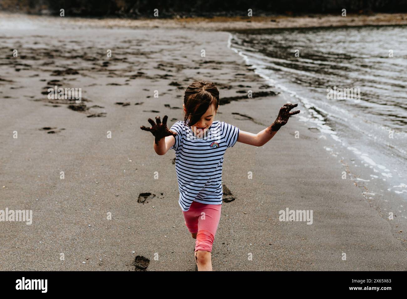 Young girl holds up muddy hands at Black Beach, New Brunswick Stock Photo