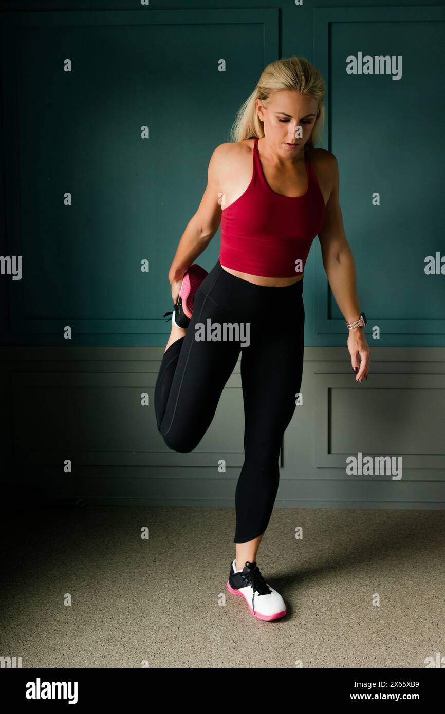 Woman stretching leg in gym with teal walls Stock Photo