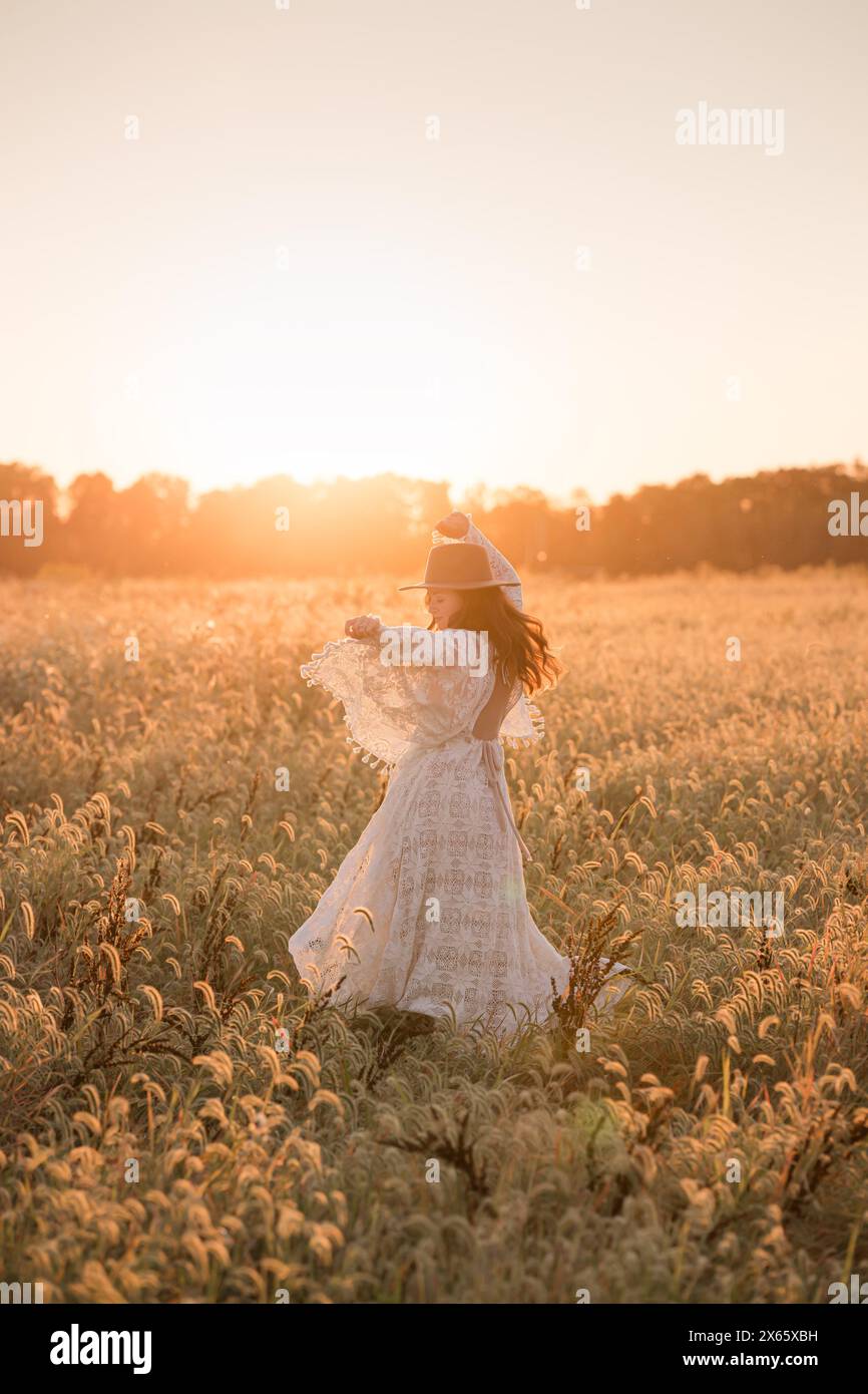 Woman in lace dress enjoying sunset in golden field Stock Photo