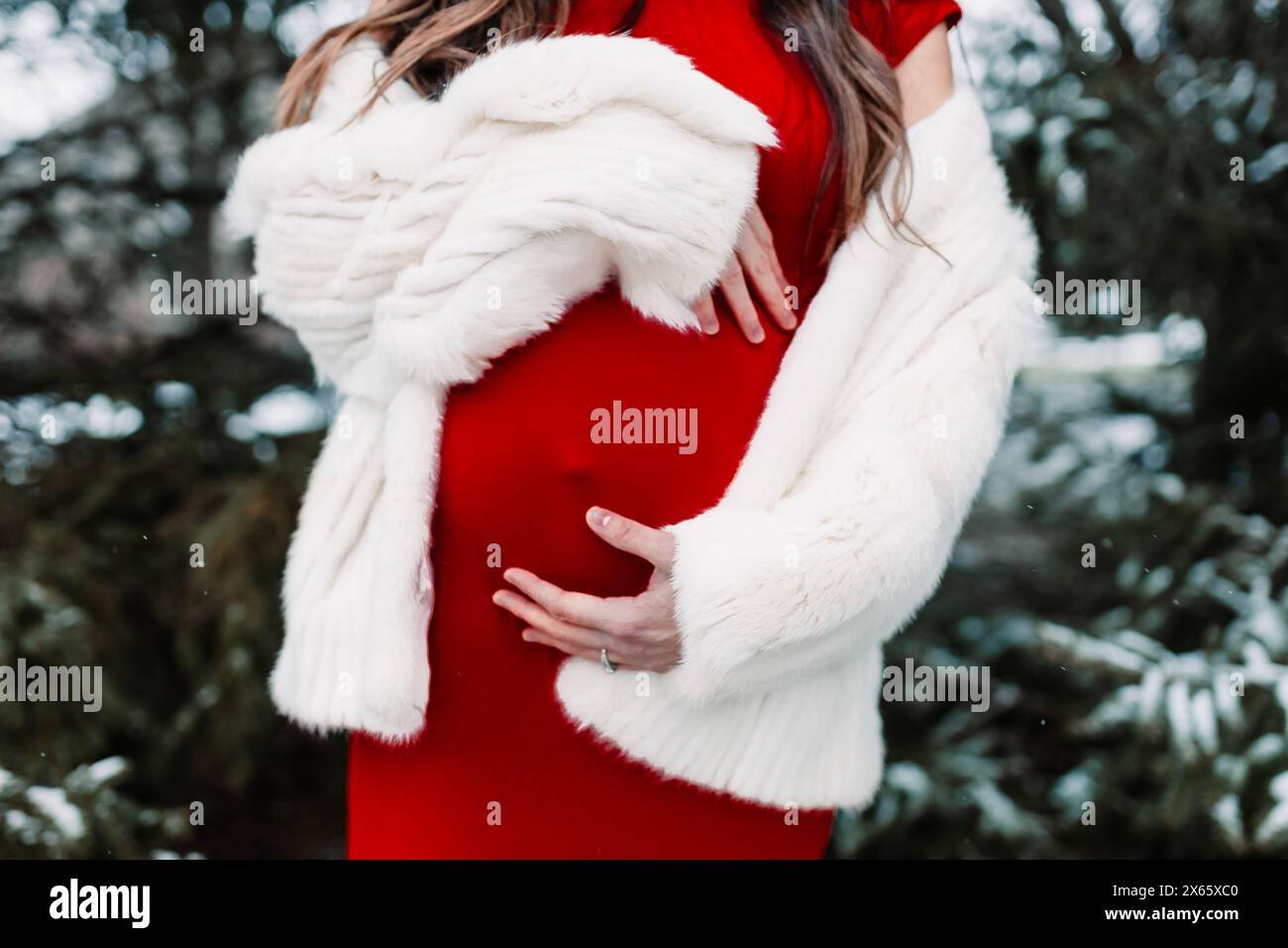 Pregnant woman in red dress with white coat in snow Stock Photo