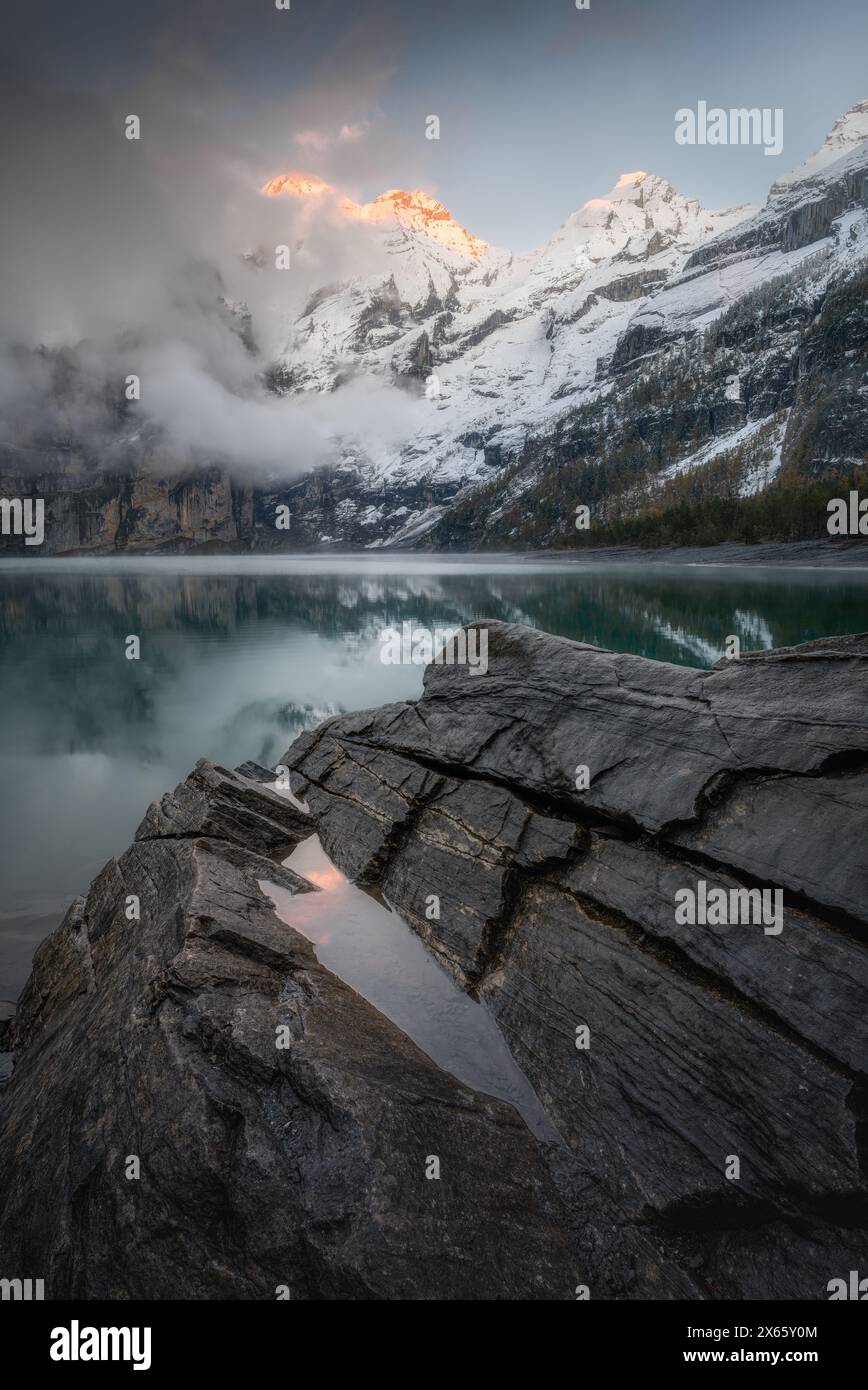 Tranquil Oeschinensee lake's Snowy Shores as Alpenglow Hits Peaks Stock Photo