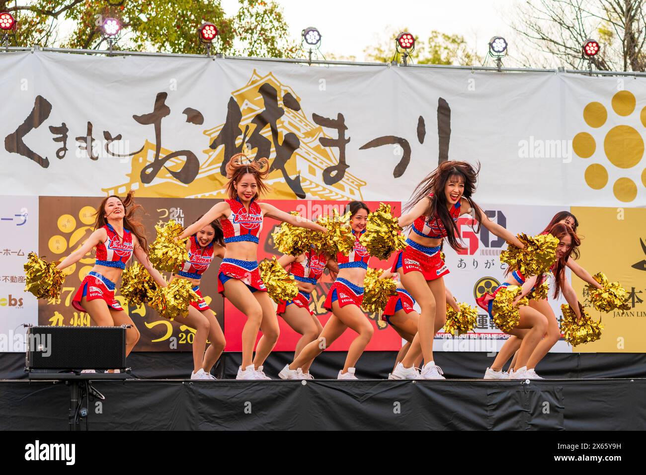 Japanese teenage women cheerleader Yosakoi dancers in tank tops and mini skirts dancing on stage holding gold glittery pom poms at the Kyusyu Gassai. Stock Photo